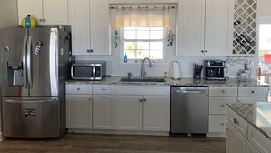 A modern kitchen with white cabinets, stainless steel appliances, a granite countertop, and a window with a striped curtain. - Gulf to Bay, on the beach home with bay access (Alligator Point)