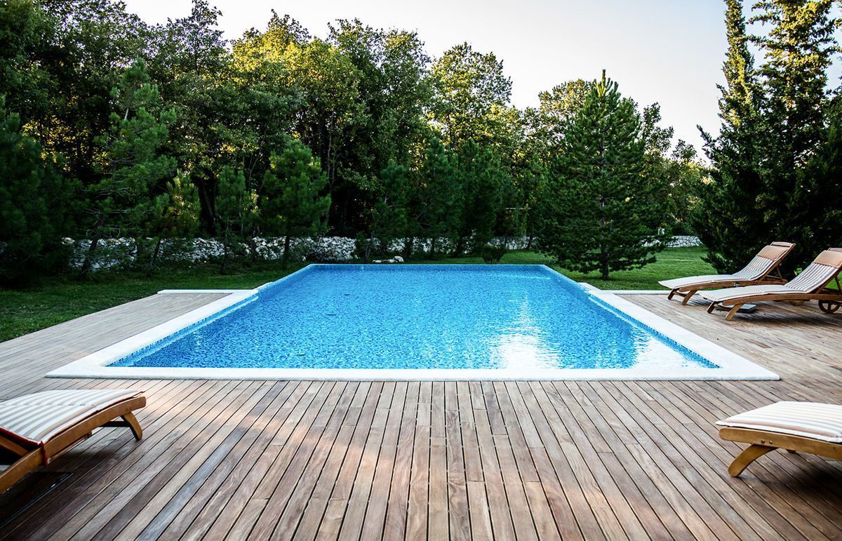 Una piscina rectangular con muelle de madera y sillas de descanso.