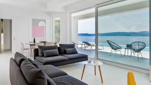 A modern living room with a large sofa, a dining area, and a balcony with a view of the sea. - Villa Dinara - Three Bedroom Villa, Sleeps 6 (Mimice)