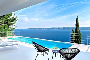 A poolside area with a view of the sea, two lounge chairs, and a table with drinks. - Villa Dinara - Three Bedroom Villa, Sleeps 6 (Mimice)