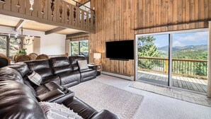 Ein geräumiges Wohnzimmer mit einer großen Ledersitzgruppe, einem flachbildfernseher an der Wand und einem Balkon mit Panoramablick auf die Berge.