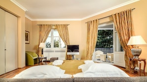 Ein Hotelzimmer mit Bett, Fernseher, Sofa, Sessel und einem Balkon mit Vorhängen.