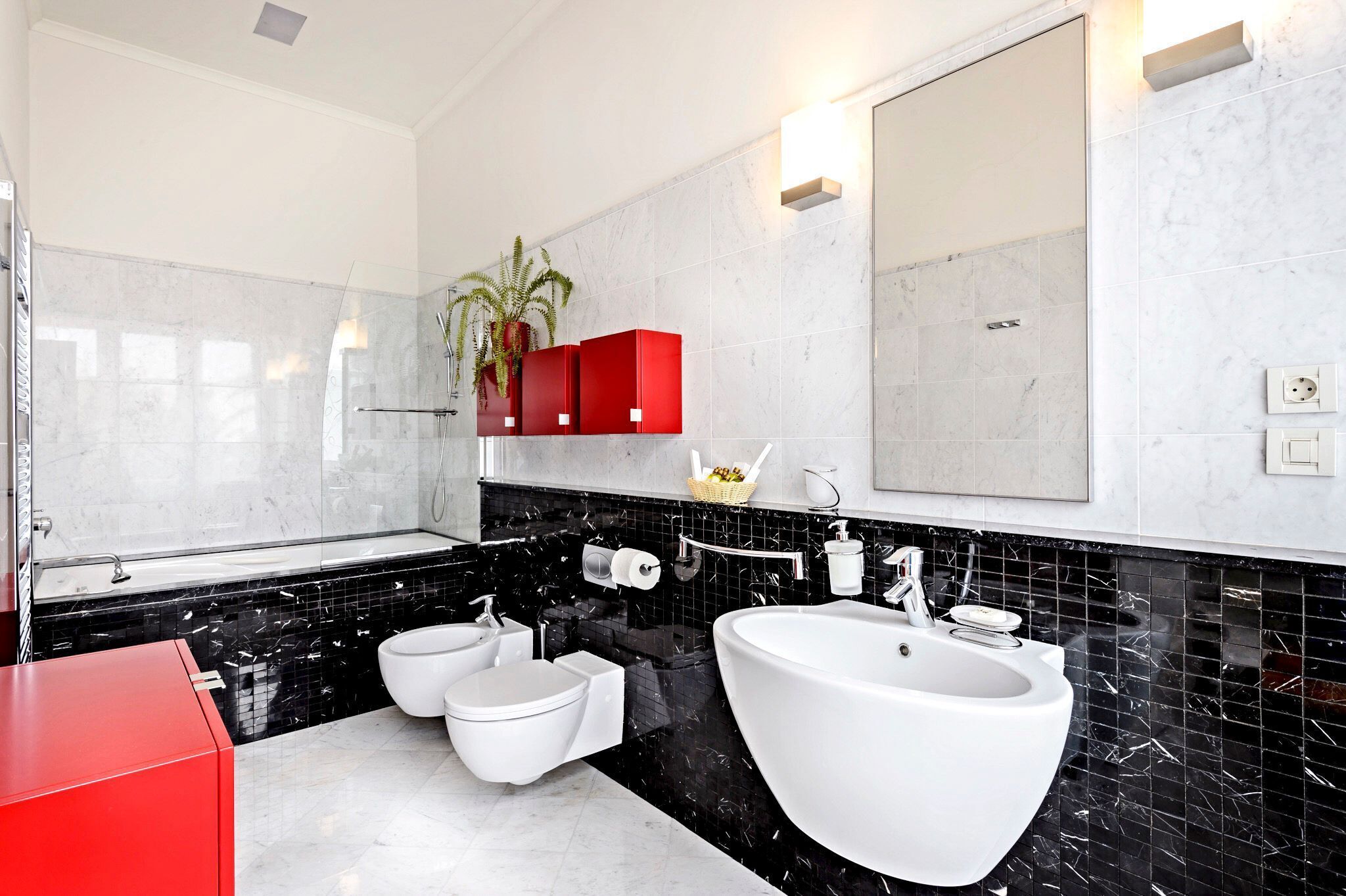 Une salle de bain moderne avec un grand lavabo blanc, deux toilettes, un meuble rouge et un miroir.