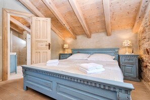 Een slaapkamer met een groot bed, houten balken in het plafond, stenen muren en twee nachtkastjes met lampen.