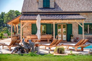 Een stenen huis met een pannendak, houten meubels en groene luiken.