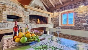 A rustic stone fireplace with a fire, a table with a fruit bowl, wine bottles, and glasses. - Old Town Villa Hvar - Five Bedroom Villa, Sleeps 12 (Uvala Tatinja)