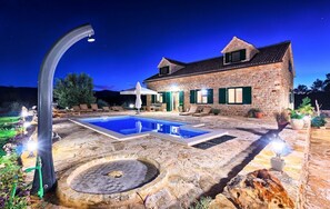 Une maison en pierre avec une piscine, un espace salon extérieur et un foyer.