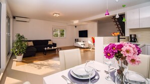 A modern living space with a dining area, a sofa, a coffee table, and a TV in the background.
