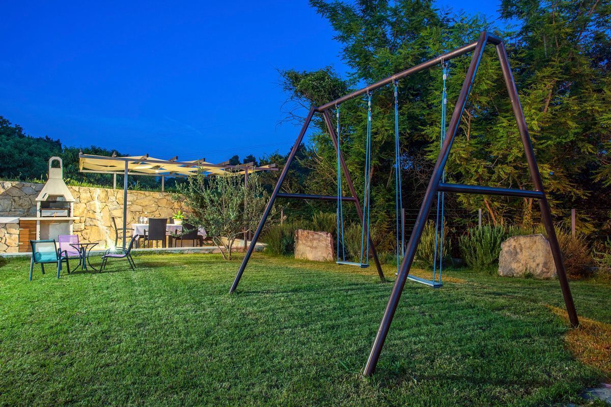 A backyard with a swing set, a barbecue area, and a stone wall.