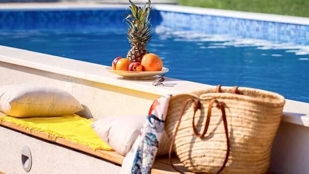 A poolside setting with a pineapple, oranges, and a woven basket.