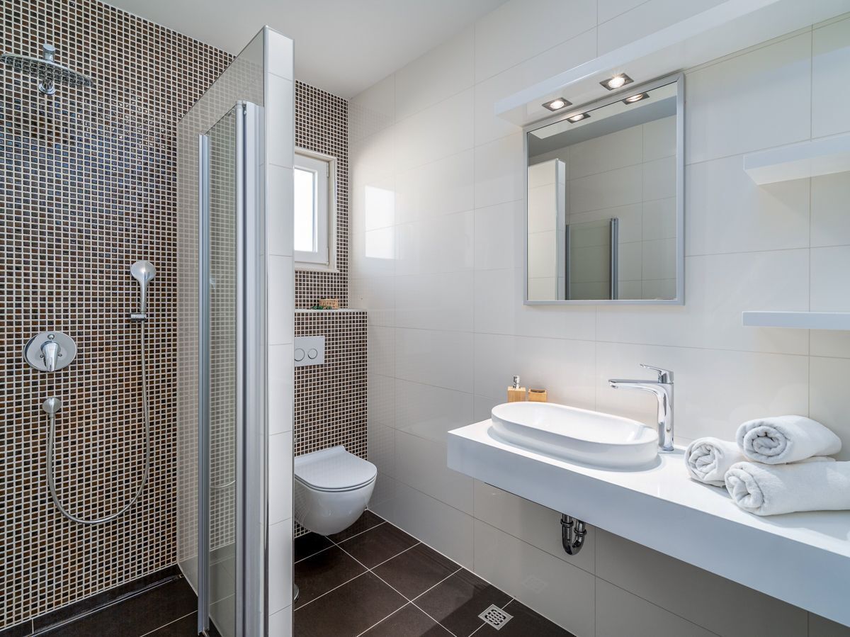 Een moderne badkamer met een douchecabine van glas, een wit wastafelmeubel en een toilet.
