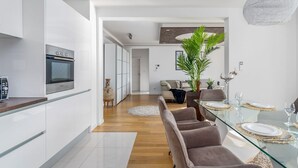 A modern kitchen with white cabinetry, a built-in oven, and a dining area with a glass table and cushioned chairs.