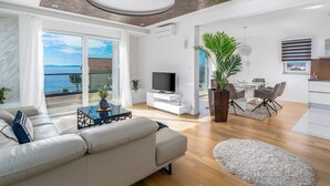A modern living room with a large sofa, a TV, and a dining area with chairs and a table.