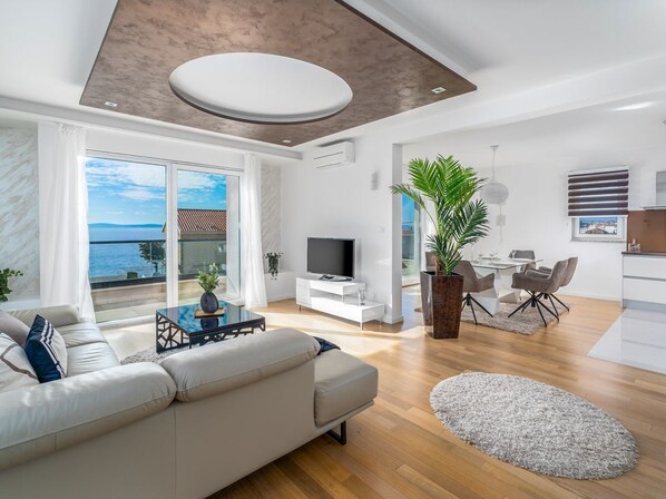 A modern living room with a large sofa, a TV, and a dining area with chairs and a table.