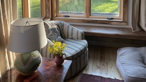 Ein gemütliches Zimmer mit großem Fenster, einer gepolsterten Bank, einer Lampe und einem Blumenstrauß.