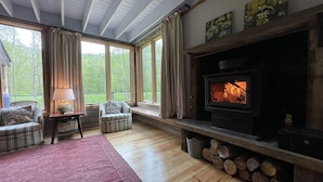 Ein gemütliches Wohnzimmer mit Kamin, großen Fenstern und einer bequemen Sitzecke.