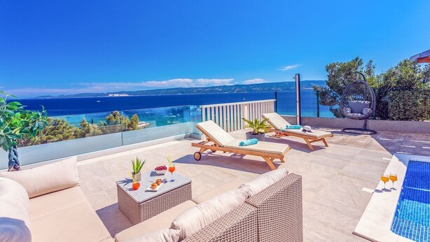 A rooftop terrace with lounge chairs, a small table with drinks, and a pool.
