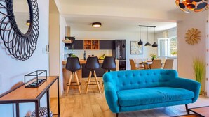 A modern living room with a teal sofa, wooden flooring, and a dining area with black chairs and a wooden table.