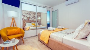 A modern hotel room with a bed, a sofa, a chair, a small table, and a large mirror.