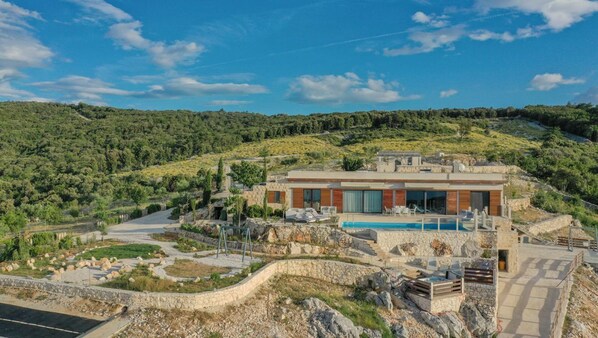 En moderne villa med swimmingpool, omgivet af anlagt have og et bakket landskab.