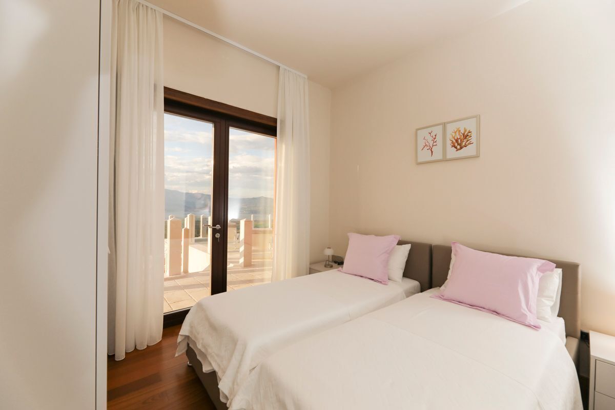 A bedroom with two beds, a balcony, and a city view.