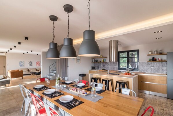 Una cocina moderna con una isla central, iluminación colgante y una zona de comedor con sillas rojas.
