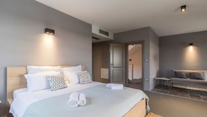 Moderni hotellihuone, jossa on suuri sänky, sohva ja kaksi seinälle asennettua valaisinta.
