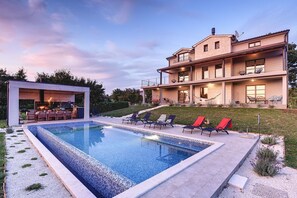 Una casa moderna de dos pisos con piscina, mobiliario de exterior y un jardín cuidado.