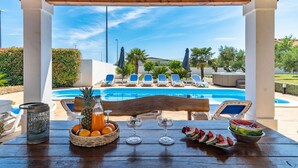 A poolside area with a wooden pergola, lounge chairs, and a table with fruit and drinks. - Villa Novi - Five Bedroom Villa, Sleeps 12 (Rudine)