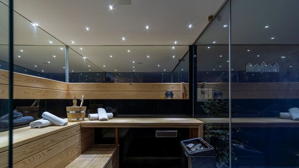 A modern sauna with wooden benches, a wooden table with towels, and a glass wall offering a view of the cityscape. - Villa Novi - Five Bedroom Villa, Sleeps 12 (Rudine)