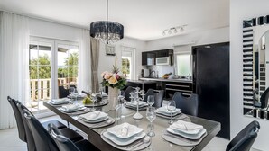 A modern dining room with a long table set for six, a chandelier, and a view of the outdoors. - Villa Novi - Five Bedroom Villa, Sleeps 12 (Rudine)