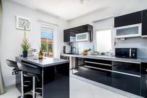 Een moderne keuken met zwart-wit kastjes, een centraal eiland met barstoelen, een magnetron en een koffieapparaat.