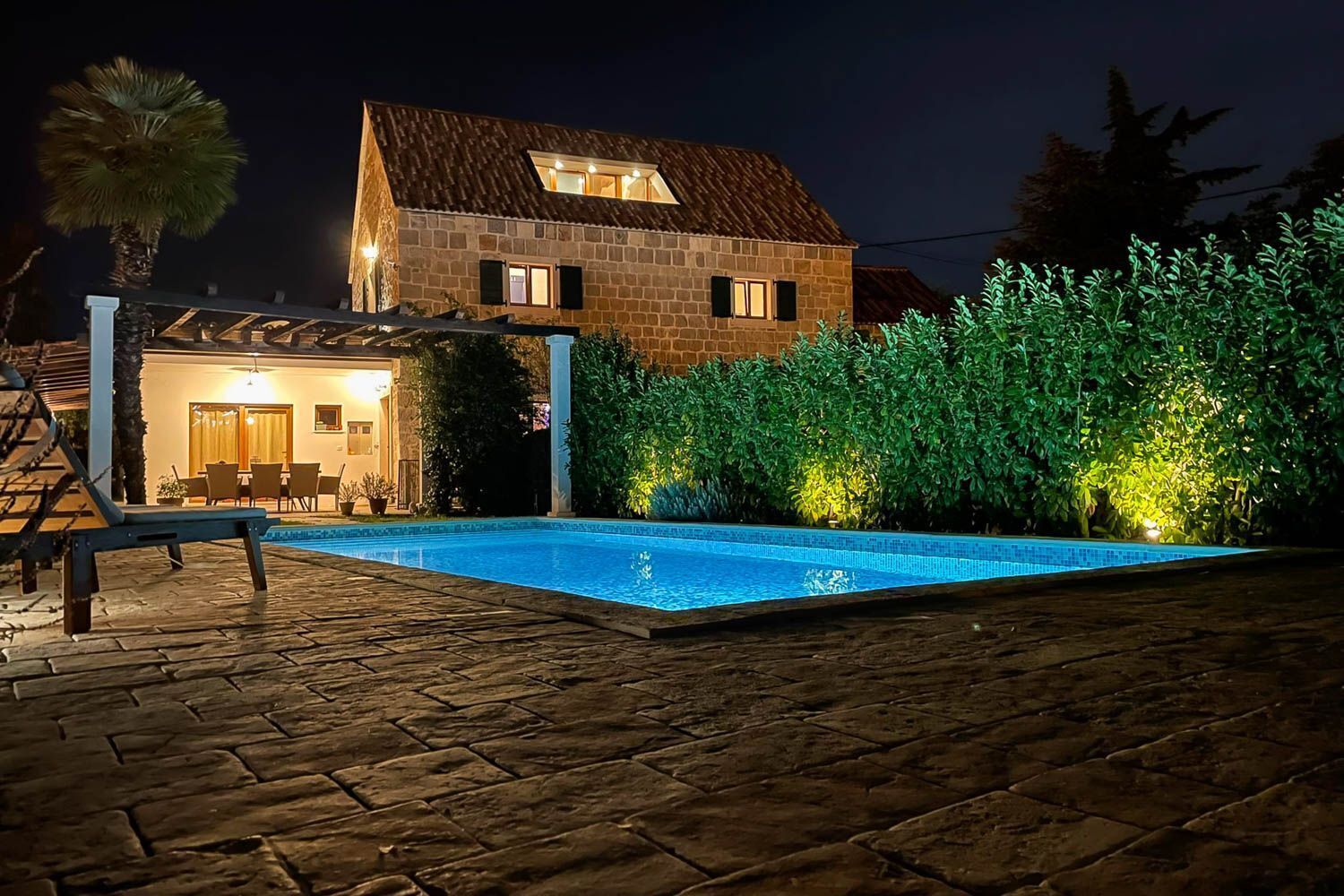 A stone house with a swimming pool, a patio area, and a well-lit interior.