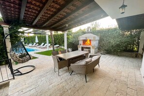 An outdoor patio with a stone table and wicker chairs, a hanging chair, and a stone fireplace. - Villa Luba - Three Bedroom Villa, Sleeps 6 (Solin)