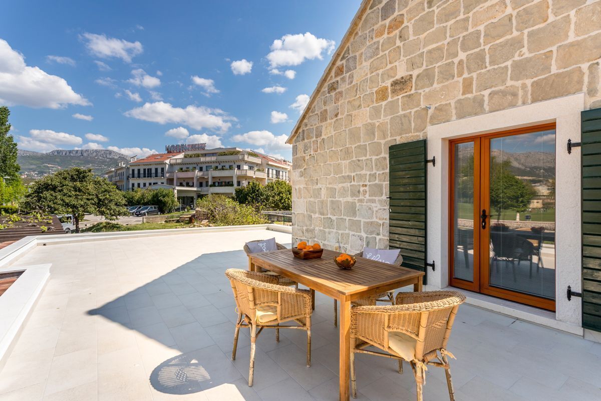 Un bâtiment en pierre avec une table en bois et des chaises en osier sur une terrasse.