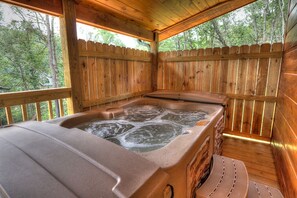 En træhytte med jacuzzi, træterrasse og udsigt til skoven.