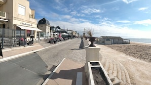 Una playa con un paseo pavimentado, un café y vista al mar.