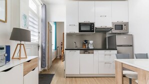 Una cocina moderna con armarios blancos, microondas, cafetera y refrigerador.