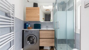 Un baño moderno y funcional con lavadora, lavamanos y cabina de ducha de vidrio.
