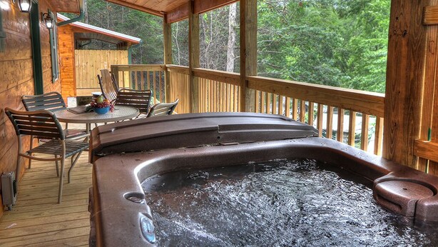 A wooden deck with a hot tub, chairs, and a table. - Hook, Line & Sinker: Perfect Cabin Nestled in Woods Only Minutes from Gatlinburg Strip (Gatlinburg)