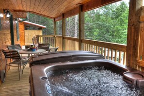 Een houten terras met een jacuzzi, stoelen en een tafel.