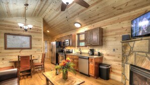 A cozy cabin-style interior with a wooden ceiling, a dining area with a table and chairs, a kitchen with modern appliances, and a fireplace. - Hook, Line & Sinker: Perfect Cabin Nestled in Woods Only Minutes from Gatlinburg Strip (Gatlinburg)