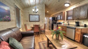 A cozy cabin interior with a wooden dining area, a leather sofa, and a kitchen with wooden cabinets and appliances. - Fish Tales: Cozy Cabin Perfect for Family Getaway (Gatlinburg)