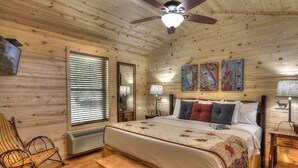 A cozy cabin-style bedroom with a large bed, wooden walls, a ceiling fan, and a window with blinds. - Fish Tales: Cozy Cabin Perfect for Family Getaway (Gatlinburg)