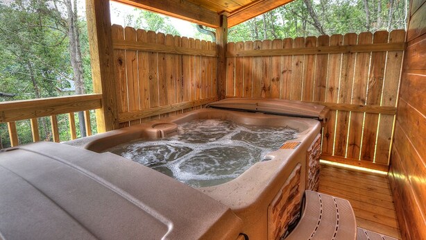A wooden cabin with a hot tub, wooden deck, and a view of the forest. - Fish Tales: Cozy Cabin Perfect for Family Getaway (Gatlinburg)