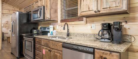 A kitchen with wooden cabinets, stainless steel appliances, a granite countertop, and a window with blinds.