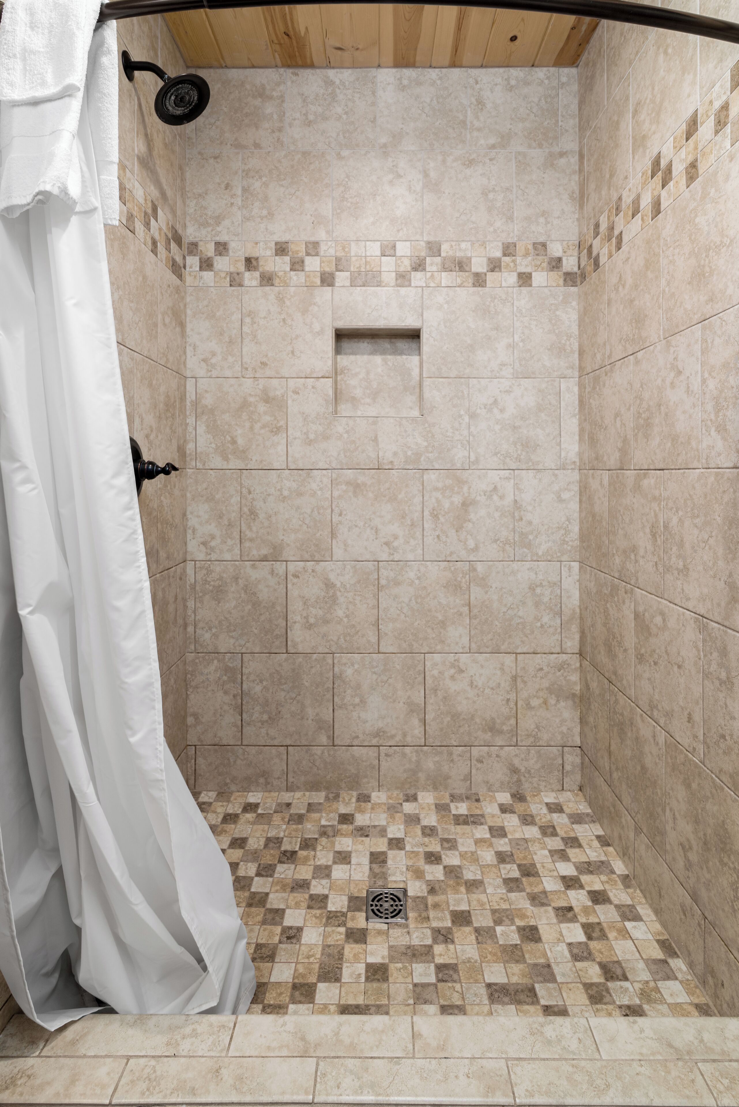 A shower area with beige tiles, a checkered floor pattern, and a white shower curtain.