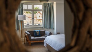 A bedroom with a bed, a sofa, a lamp, and a view of buildings outside the window. - The Ship Inn (Holt)