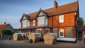 A traditional brick building with a gabled roof and multiple windows. There are four wooden barrels in front of the building. - The Ship Inn (Holt)