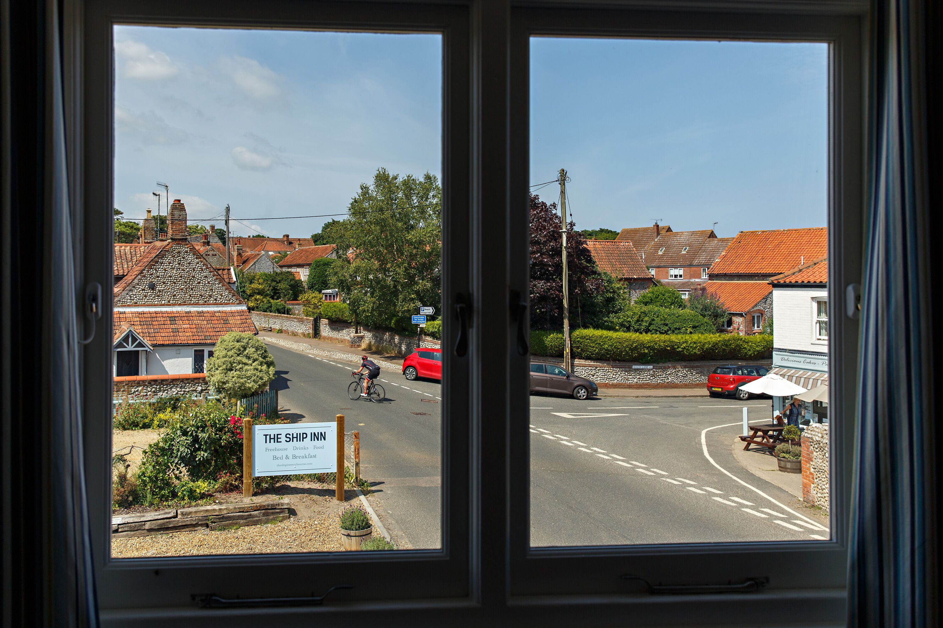 A view from a window of a street with a sign for 'The Ship Inn' and a red car parked on the side.